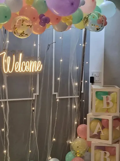 A close-up of the pastel welcome decor, highlighting the "Welcome" neon sign, fairy light curtain, and the "BABY" blocks, which are great for photos.