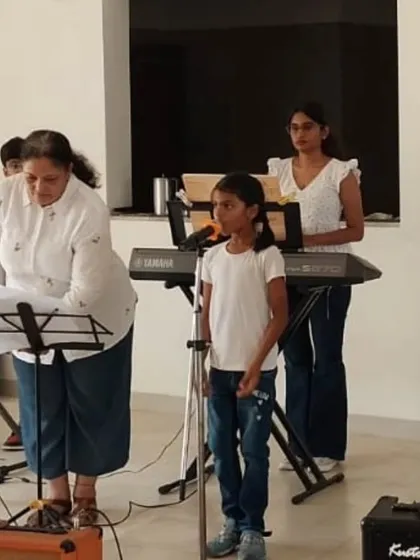 A teacher guides a young vocalist at the microphone during a performance. This highlights our supportive, hands on teaching style.