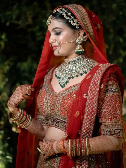 A beautiful outdoor bridal portrait, with the bride adjusting her veil against a lush green background.