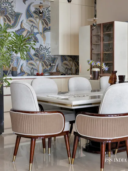 A bold, patterned wallpaper serves as a stunning backdrop for this dining area. The neutral, upholstered chairs with brass-tipped legs add a touch of mid-century modern glamour.
