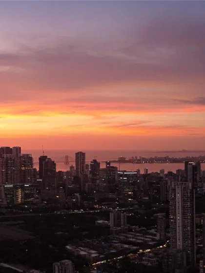 The Bandra-Worli Sea Link is visible in the distance as the sun sets over Mumbai, painting the sky in vibrant shades of orange and pink.