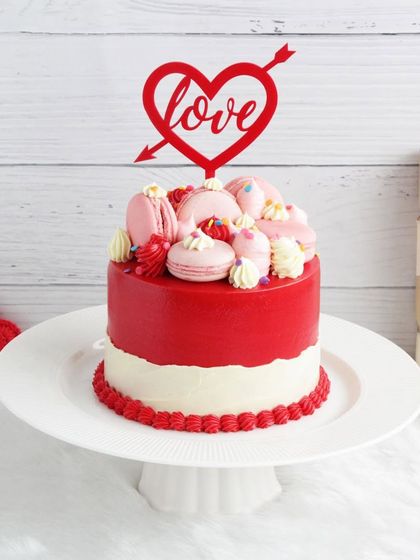 A stunning red and white Valentine's cake topped with macarons and a "Love" topper. It's a beautiful and delicious way to express your feelings.