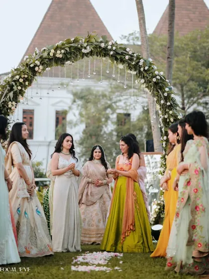 The bride shares a moment with her bridesmaids under a beautiful floral arch before the ceremony begins.