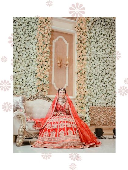 A majestic shot of the bride on a royal sofa, against a wall of flowers. The entire composition screams elegance and grandeur.