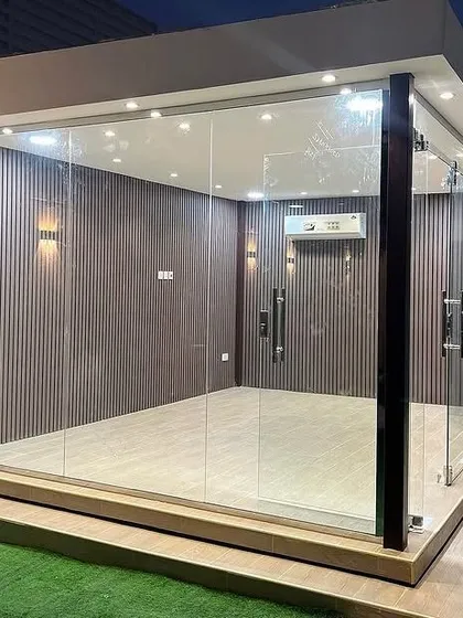 A close-up view of a finished glass garden room, highlighting the interior details. Note the vertical fluted wall panels, minimalist sconce lighting, and the installed air conditioning unit, which ensures year-round comfort in our prefab structures.