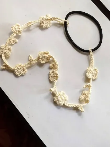 This is our crochet floral hairband in a natural, off-white color. It features a string of tiny handmade flowers attached to a simple elastic tie for an easy fit.