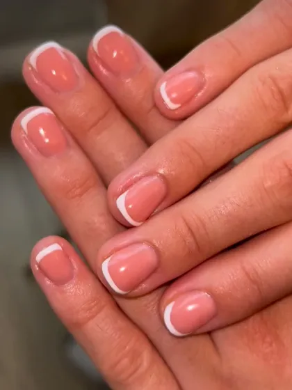 A classic French manicure on shorter, natural nails with a peachy-pink base. This look is perfect for everyday elegance and professionalism.