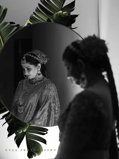 A creative black and white bridal portrait using a mirror for a reflective, introspective shot. The composition with tropical leaves adds an artistic and modern touch to the classic portrait.