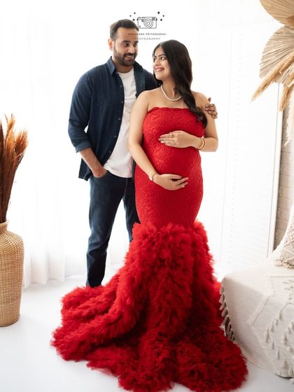 A classic couple's portrait from a studio maternity session. The combination of the red gown and casual denim creates a stylish and balanced look.