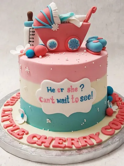 A classic gender reveal cake with pink and blue tiers, topped with a baby carriage, bottle, and booties.