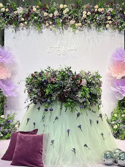 For baby Ayzah's cradle ceremony, we designed this breathtaking floral masterpiece. The decor features a custom tulle skirt for the main table, overflowing with fresh purple and lilac flowers, set against a clean white backdrop with a personalized name sign.