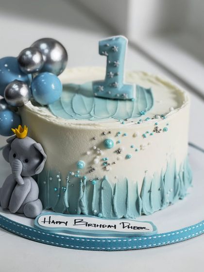 Such a sweet way to celebrate turning one! This cake features soft blues, a tiny, crowned elephant, and shimmering silver details, making a first birthday truly magical.