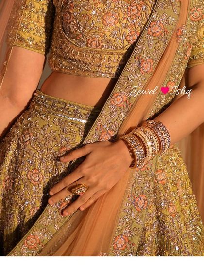 A mid-shot focusing on the intricate details of the lehenga and the stacked Polki bangles on the bride's wrist.