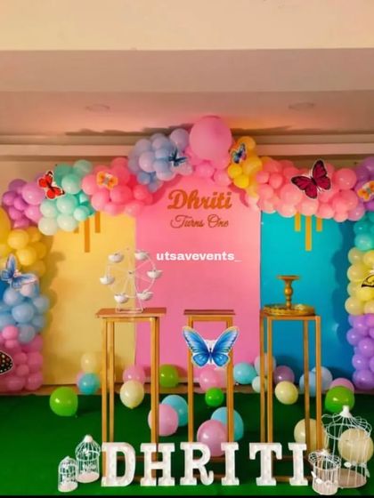A colorful butterfly-themed first birthday with a pastel rainbow balloon arch. This vibrant setup includes multiple butterfly accents and custom name lettering, creating a cheerful party atmosphere.