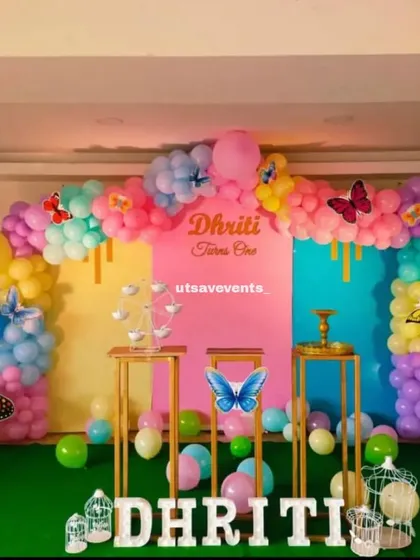 A whimsical butterfly-themed first birthday. The decor features a colorful panel backdrop, butterfly cutouts, and a multi-colored balloon arch.