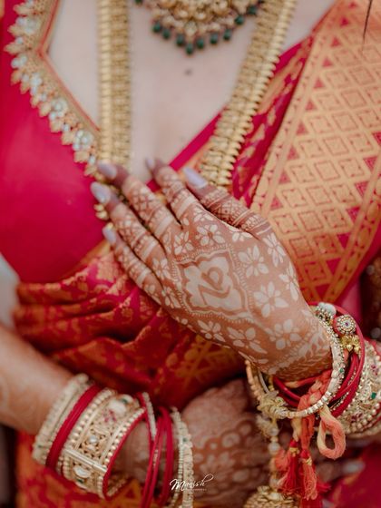A detailed shot of the bride's hands, adorned with beautiful white henna and traditional red and white bangles.