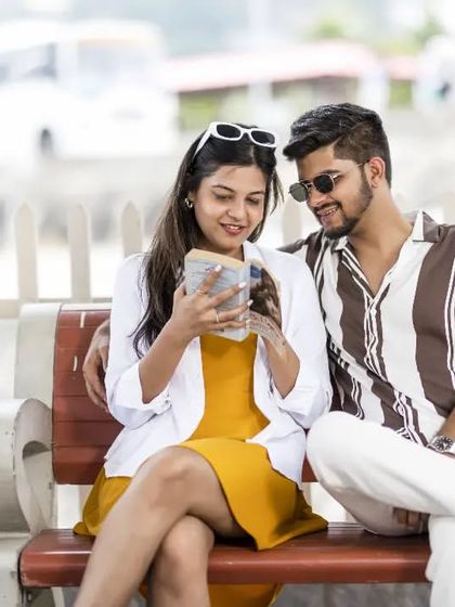 A sweet, everyday moment of the couple looking at a phone together while sitting on a bench. It’s a relatable and authentic slice-of-life photo.