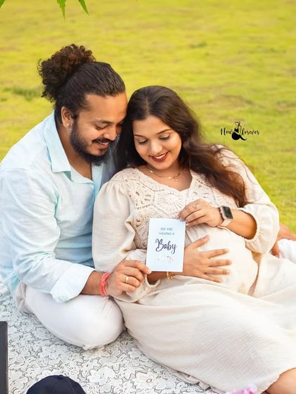 Sharing a happy secret. The couple looks down at a card announcing their baby, a private moment of joy captured during their outdoor session.