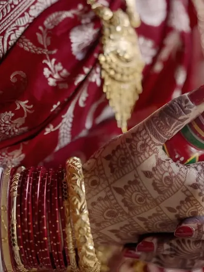 The beauty of a wedding is in its details. This close-up captures the bride's hands, adorned with intricate mehndi and traditional Bengali bangles, holding the ceremonial 'Gach Kouto', a symbol of prosperity and happiness.