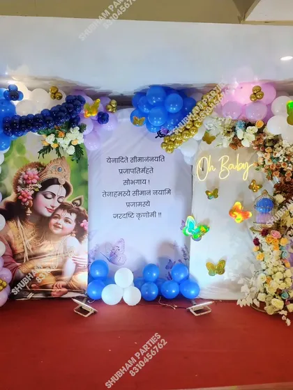 A traditional baby shower or naming ceremony setup with a Krishna-themed backdrop and an "Oh Baby" neon sign.