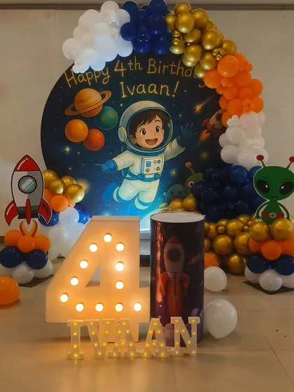 I designed this exciting outer space theme for a 4th birthday, complete with an astronaut backdrop and planets. The decor includes a large light-up number '4', rocket and alien balloon sculptures, and a color-coordinated balloon arch.