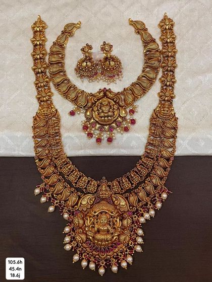 A complete bridal set in 92.5 silver with gold plating, including a choker and a long haram. Both pieces feature beautiful temple designs with goddess motifs and are adorned with pearls and red stones.