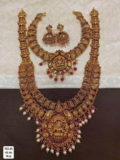 A complete bridal set in 92.5 silver with gold plating, including a choker and a long haram. Both pieces feature beautiful temple designs with goddess motifs and are adorned with pearls and red stones.