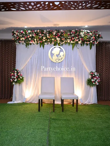 A simple yet elegant baby shower stage. The white draped backdrop is accented with a floral header and a custom cutout, creating a serene and classic look.