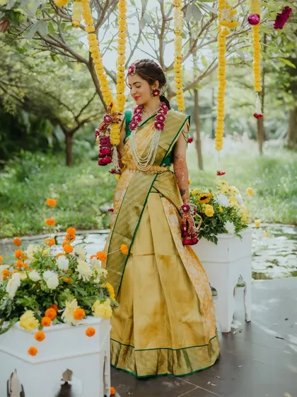 A full-length portrait of the bride, looking radiant in her Haldi attire, surrounded by marigold decorations.