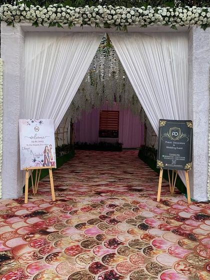This entrance gate features a clean, modern design with white floral walls and a draped entryway. We placed custom welcome signs for the couple on either side to add a personal touch.
