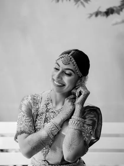 A classic black and white bridal portrait. The bride's joyful expression as she puts on her earring is a timeless moment captured beautifully.