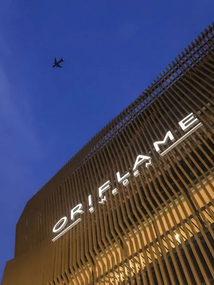 A dramatic low-angle shot of the Oriflame office facade against the evening sky. The illuminated signage and the texture of the slatted aluminum structure create a powerful brand statement.