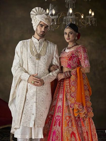 A regal portrait of a groom and bride. The groom's ivory sherwani, with its detailed embroidery and matching safa, perfectly complements the bride's attire, creating a picture of coordinated elegance.