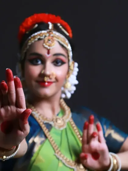 This portrait focuses on the expressive hand mudras of Bharatnatyam. The dancer's hands are brought to the foreground, showcasing the red dye and the precision of her movements.