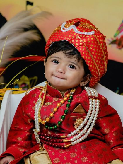 A smiling toddler in his red sherwani and turban.