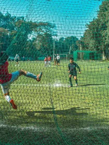 A goalkeeper makes a dramatic, leaping save, captured from behind the net.