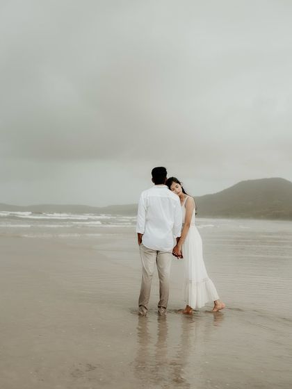 She rests her head on his shoulder as they gaze out at the waves. A quiet, comforting moment that speaks of trust and togetherness.