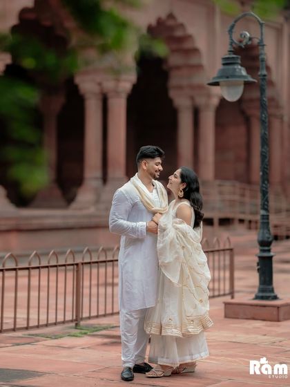 A candid moment of laughter and conversation during a pre-wedding shoot at a Delhi fort. The warm tones of the sandstone pillars and the soft light create a romantic and natural atmosphere.