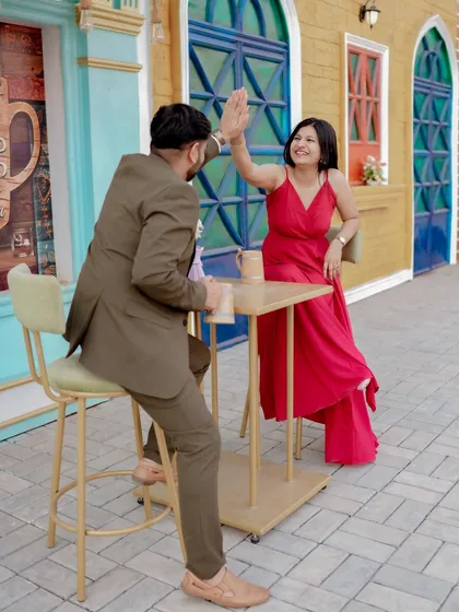 A playful moment sharing a drink against a vibrant blue door, reminiscent of a European street. The woman's bright red dress pops against the cool tones, creating a lively and stylish pre-wedding photo.