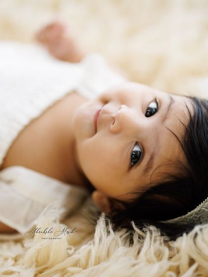 The simple beauty of a baby in white. Lying on a soft, fluffy rug, this little one looks right into the lens, creating a direct and heartwarming connection.