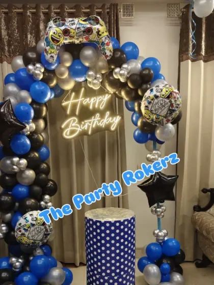 Game on! A video game-themed birthday party with a balloon arch topped with a giant controller balloon. The blue, black, and silver colors create a cool, modern look.