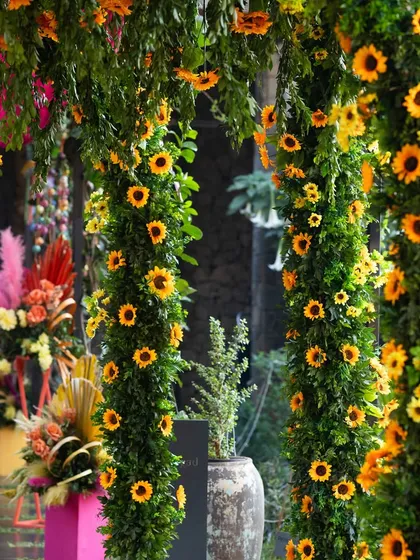 Columns wrapped in lush green garlands and dotted with bright sunflowers, creating a beautiful, natural entrance.