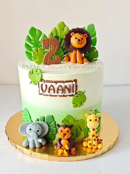 A stylish safari cake for a second birthday. This design features a subtle green ombre effect and graceful 3D animal toppers including a lion, elephant, monkey, and giraffe.