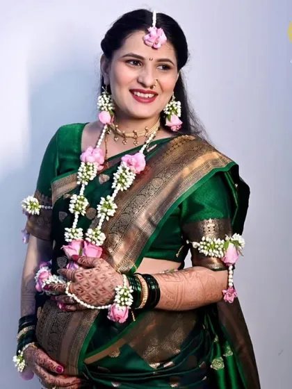A smiling portrait of an expectant mother. Her custom floral jewellery, featuring pink roses and baby's breath, adds a soft, celebratory touch to her baby shower look.