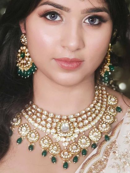A classic and elegant look featuring a multi-layered Kundan necklace with green bead drops, paired with a white and gold outfit. This shows how versatile these sets can be.