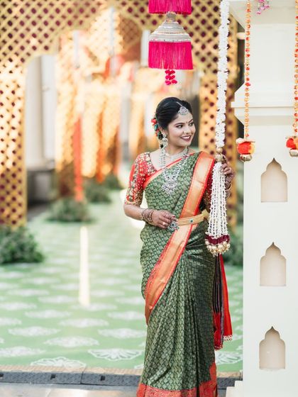 A beautiful bride in a green saree, posing elegantly in a grand, decorated hallway.