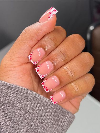 This design features a crisp white French tip decorated with a pattern of tiny red hearts. It's a bold and graphic look on a modern square nail shape.