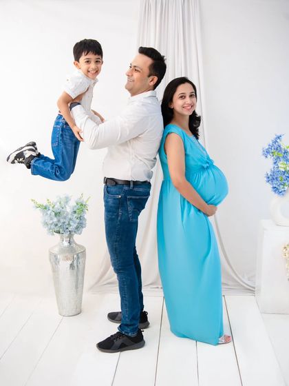 A playful and dynamic family maternity photo. The father lifts his son in the air, creating a moment of pure joy, while the mother looks on with a serene smile.