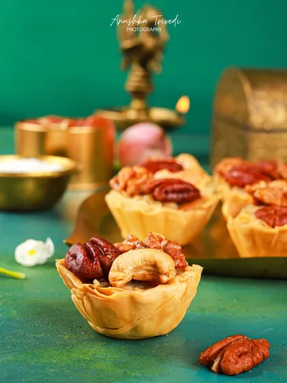 A close-up of the mini nut tartlets, showing the detail of the pecans and cashews. The moody lighting and deep teal background make the dessert look luxurious.