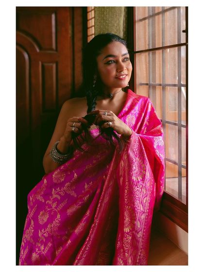 Another angle from a beautiful window-lit series. This shot shows the model looking out, her expression framed by the light, with the focus on the intricate patterns of her pink saree.